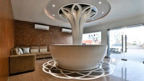 A modern lobby with a central seating area, a unique ceiling design, and a view of the street outside. - Hotel Centre Point (Mundra)