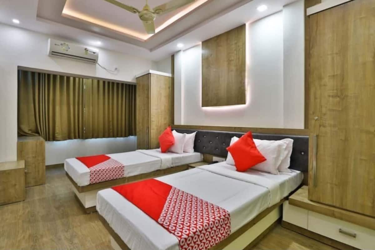 A hotel room with two beds, a ceiling fan, an air conditioning unit, and a wooden wardrobe.