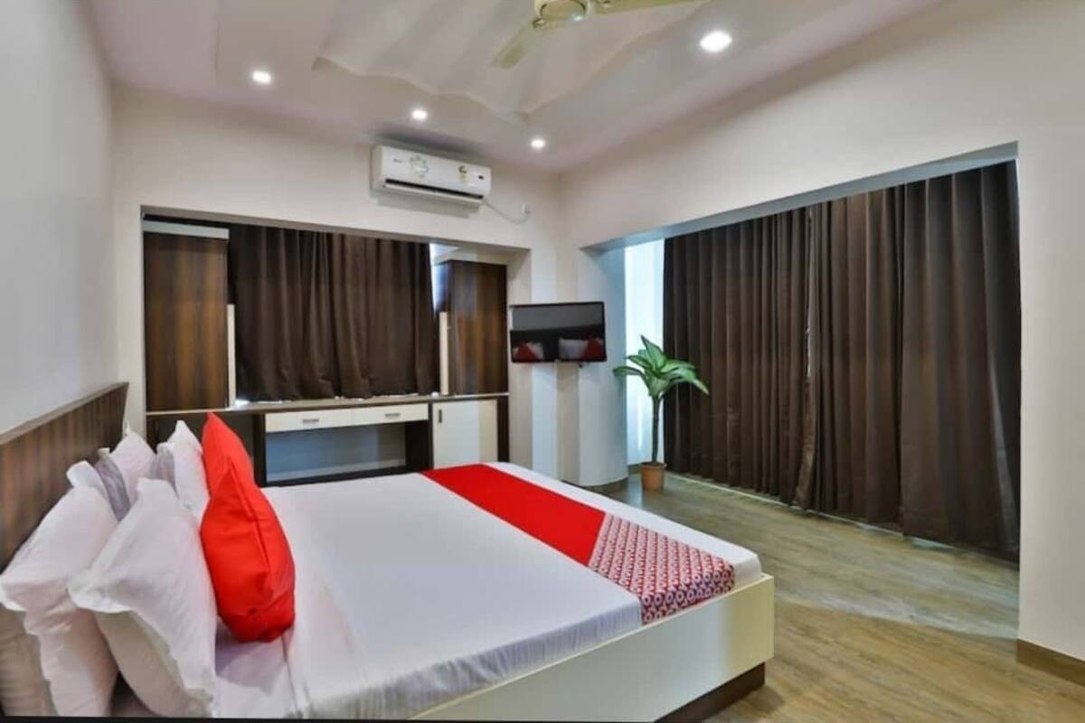 A hotel room with a bed, a desk, a chair, an air conditioner, a TV, and a window with curtains.