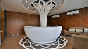 A reception area with a modern reception desk, a central light fixture, and a patterned wall. - Hotel Centre Point (Mundra)