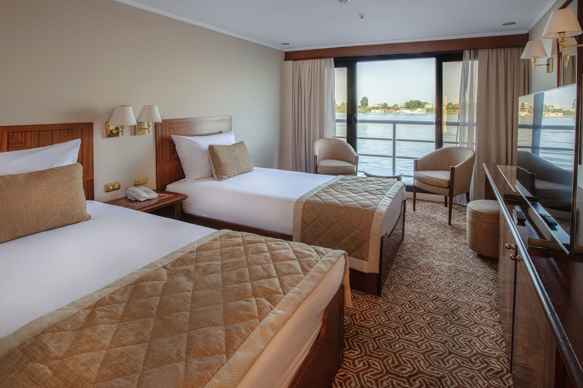 A hotel room with two beds, a TV, a chair, a desk, and a view of the water.