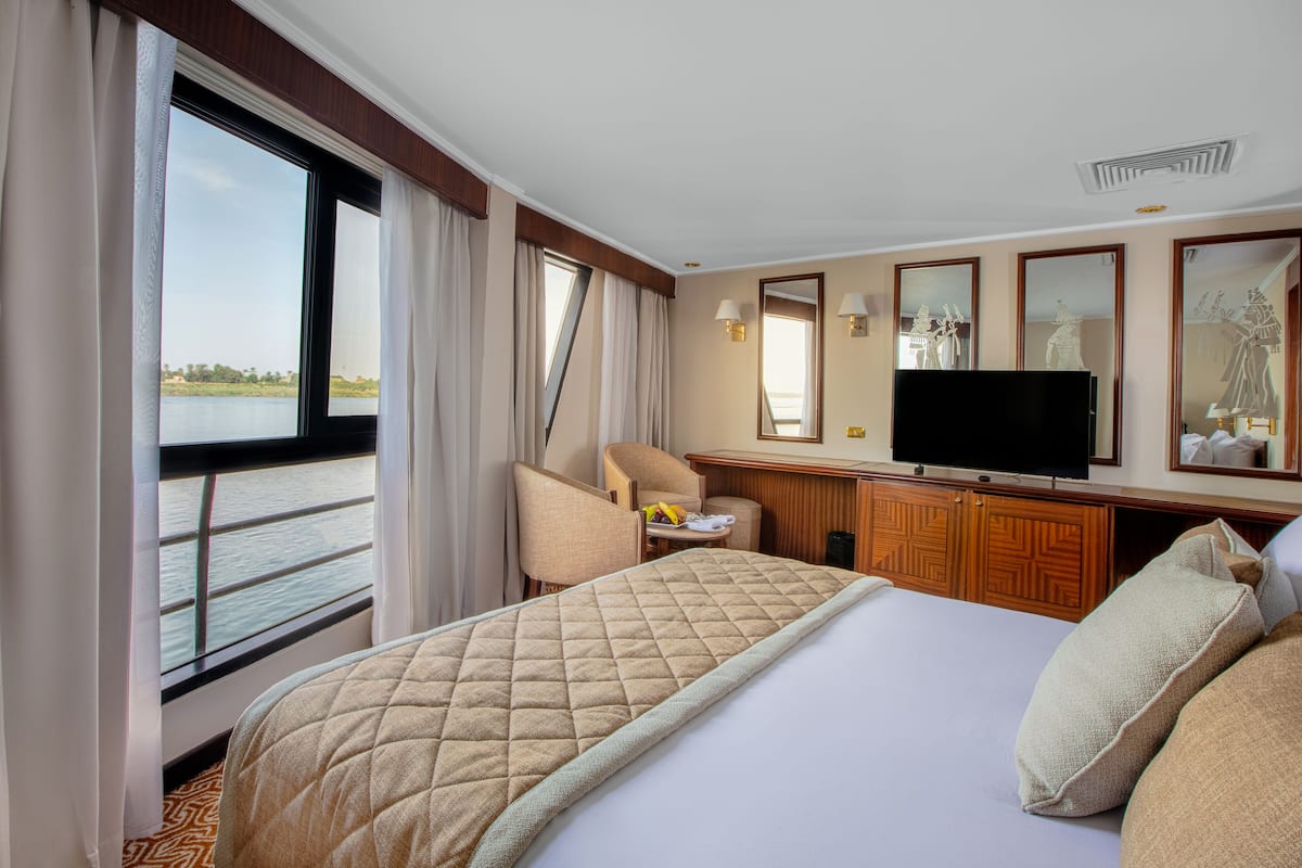 A hotel room with a large bed, a television, a desk, and a view of the water.