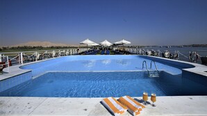 A pool area with lounge chairs and umbrellas, a clear sky, and a distant view of a body of water. - JAZ Crown Emperor Nile Cruise - Every Thursday from Luxor for 07 & 04 Nights - Every Monday from Aswan for 03 Nights (Luxor)