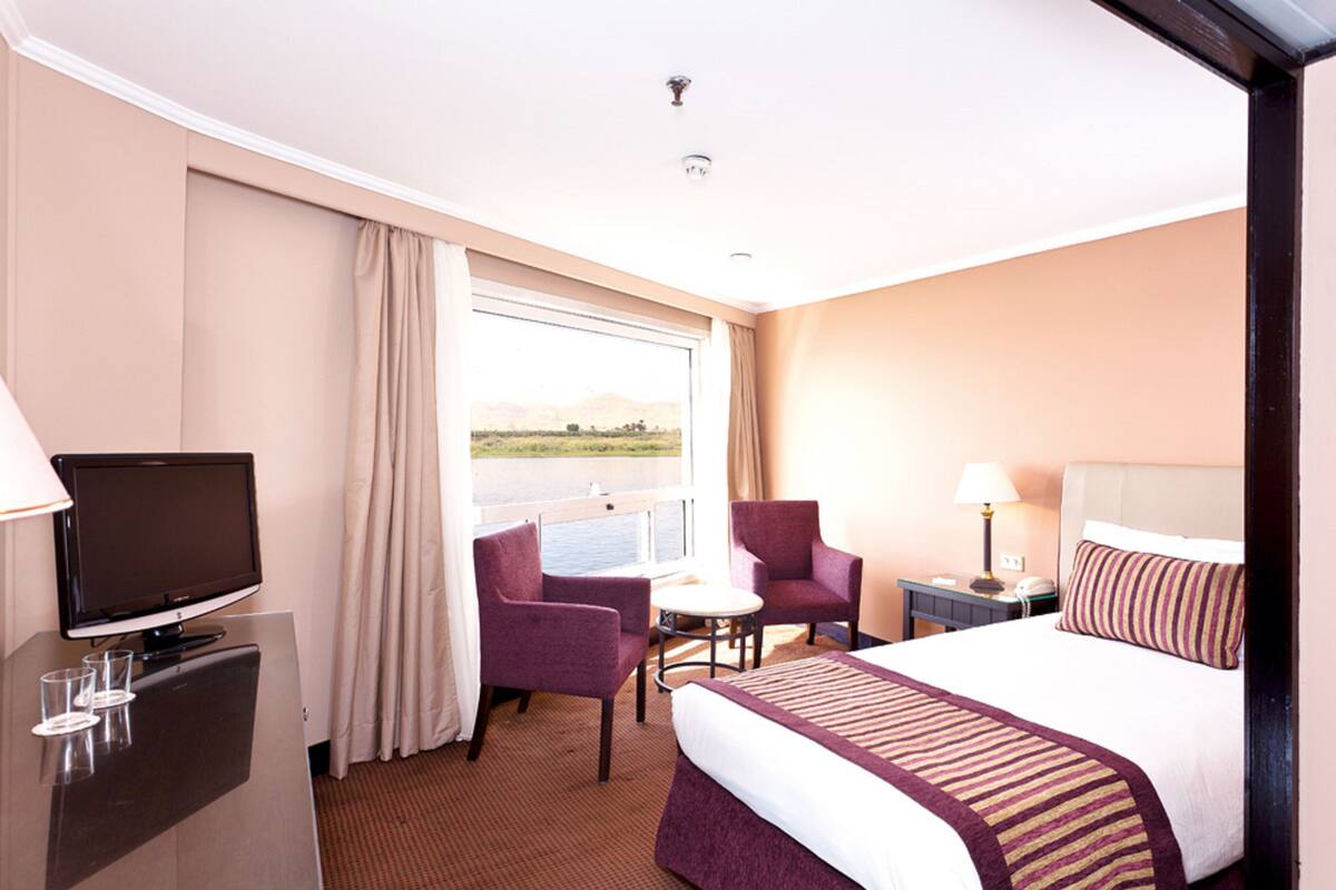 A hotel room with a bed, a TV, a desk, a chair, and a window with a view.