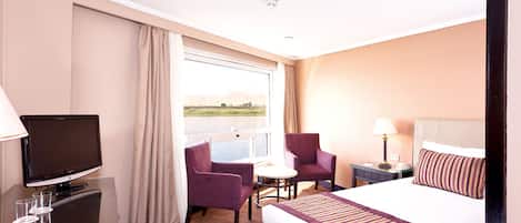 A hotel room with a bed, a TV, a desk, a chair, and a window with a view.