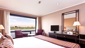 A hotel room with a large bed, a TV, a desk, and a view of a body of water. - Jaz Crown Prince Nile Cruise - Every Monday from Luxor for 07 & 04 Nights - Every Friday From Aswan for 03 Nights (Luxor)