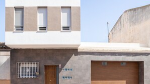 Ein Gebäude mit weißem Obergeschoss, grauem Untergeschoss, einer Holztür und vergitterten Fenstern sowie einer Garage.