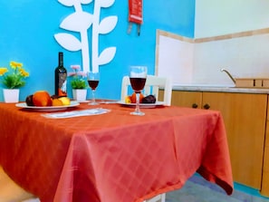 A dining table with a red tablecloth, two wine glasses, and plates of fruit. - Medusa Studios (Kefalonia)
