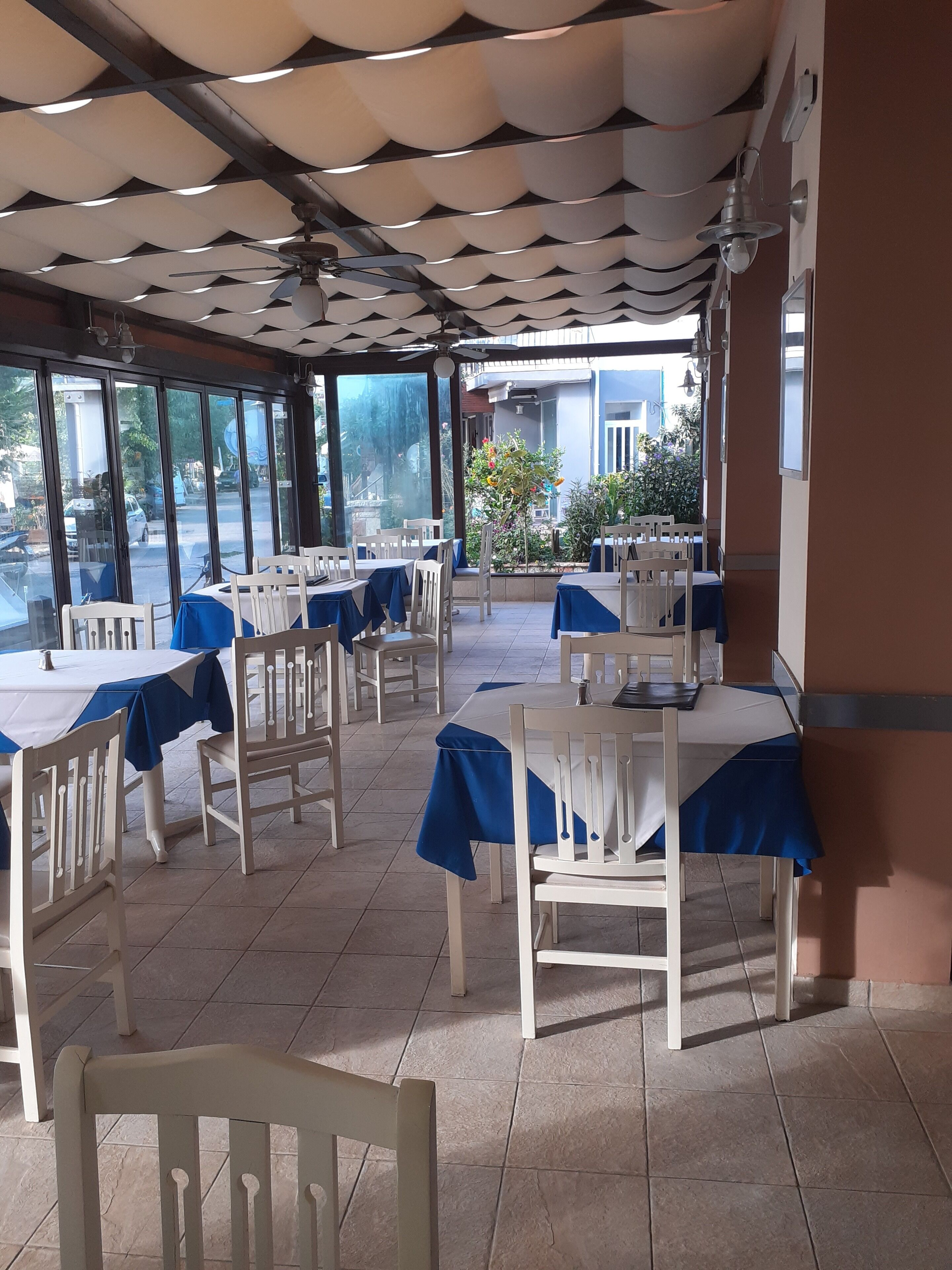 Ein Restaurant mit Tischen, die mit blauen Tischdecken bedeckt sind, weißen Stühlen und einer Decke mit einem wellenförmigen Muster.