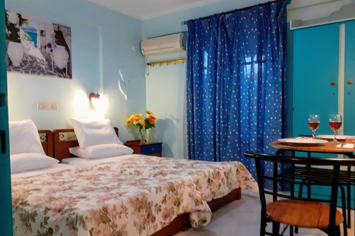 A hotel room with a bed, a desk with two glasses of wine, and a blue curtain with a polka dot pattern.