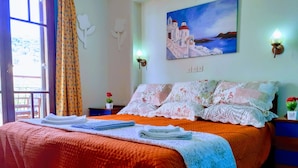 A hotel room with a bed, a painting of a coastal scene, a window with curtains, and a nightstand with a lamp. - Medusa Studios (Kefalonia)