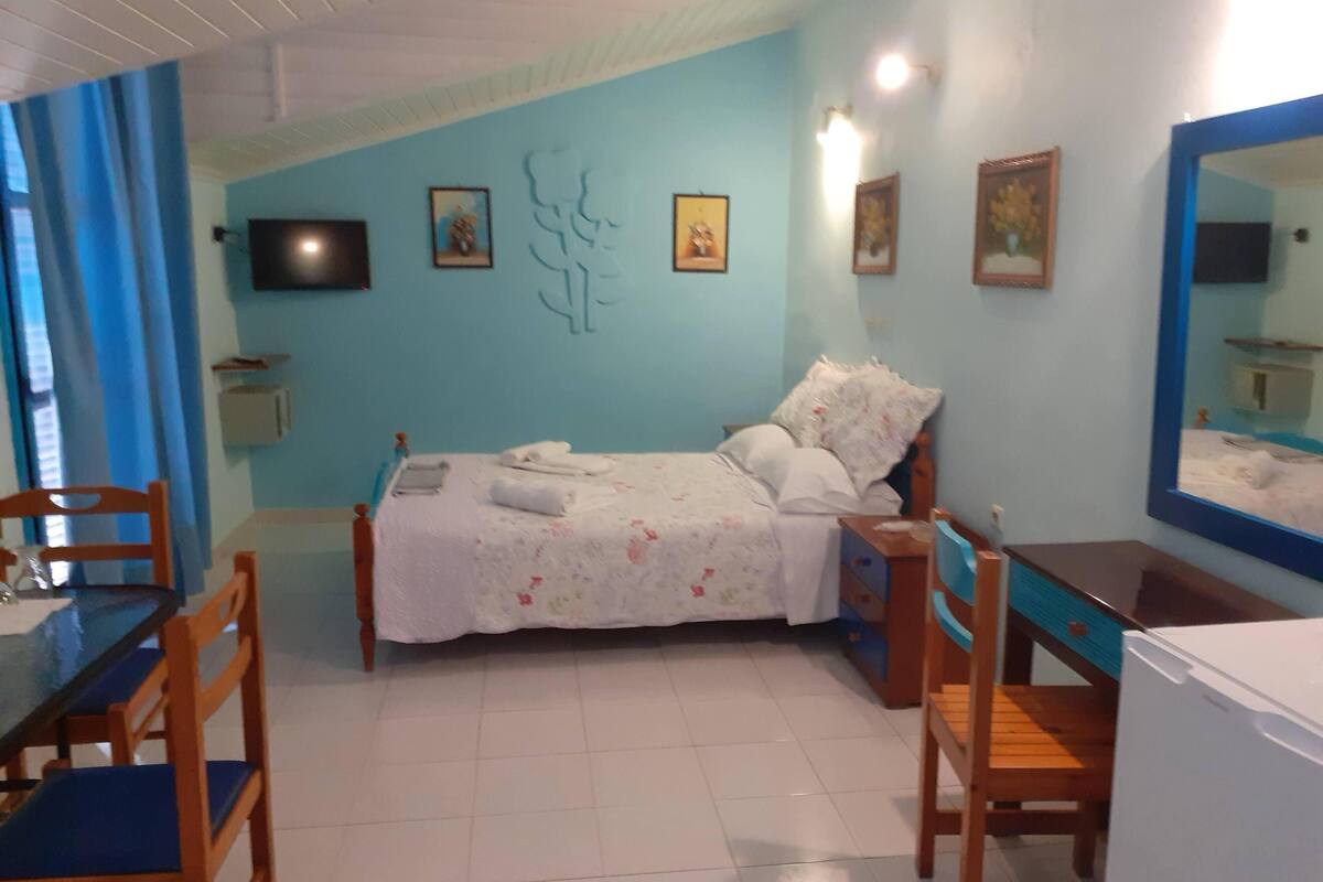 A bedroom with a bed, a desk, chairs, and a mirror.