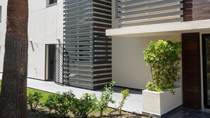 A modern building with horizontal slats, a palm tree, and a small garden area.