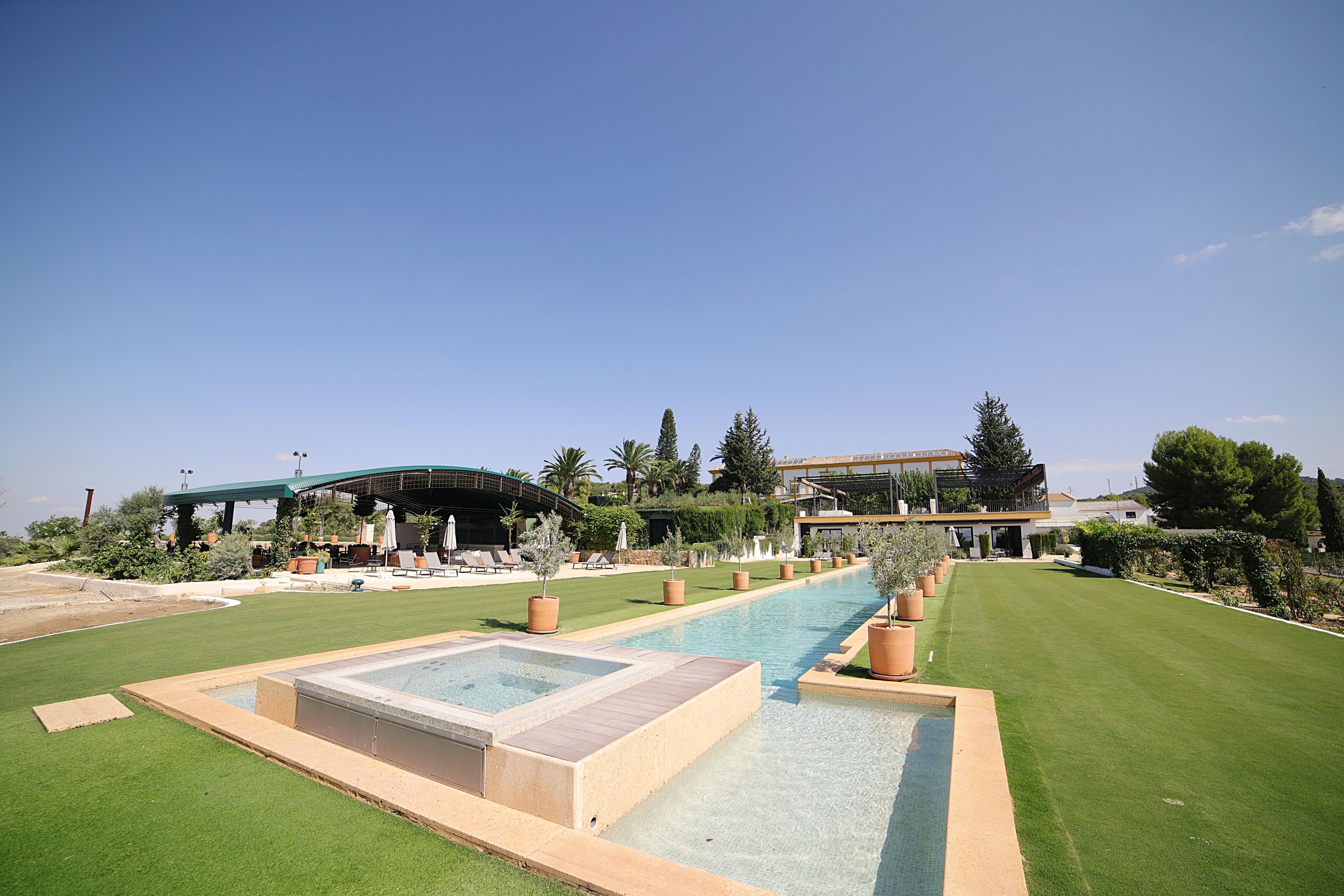 Piscina com deck de madeira, rodeada por gramados bem cuidados e plantas em vasos.