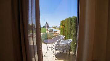 Blick durch ein Fenster auf einen Patio mit Pool, zwei weißen Stühlen und einem Tisch.