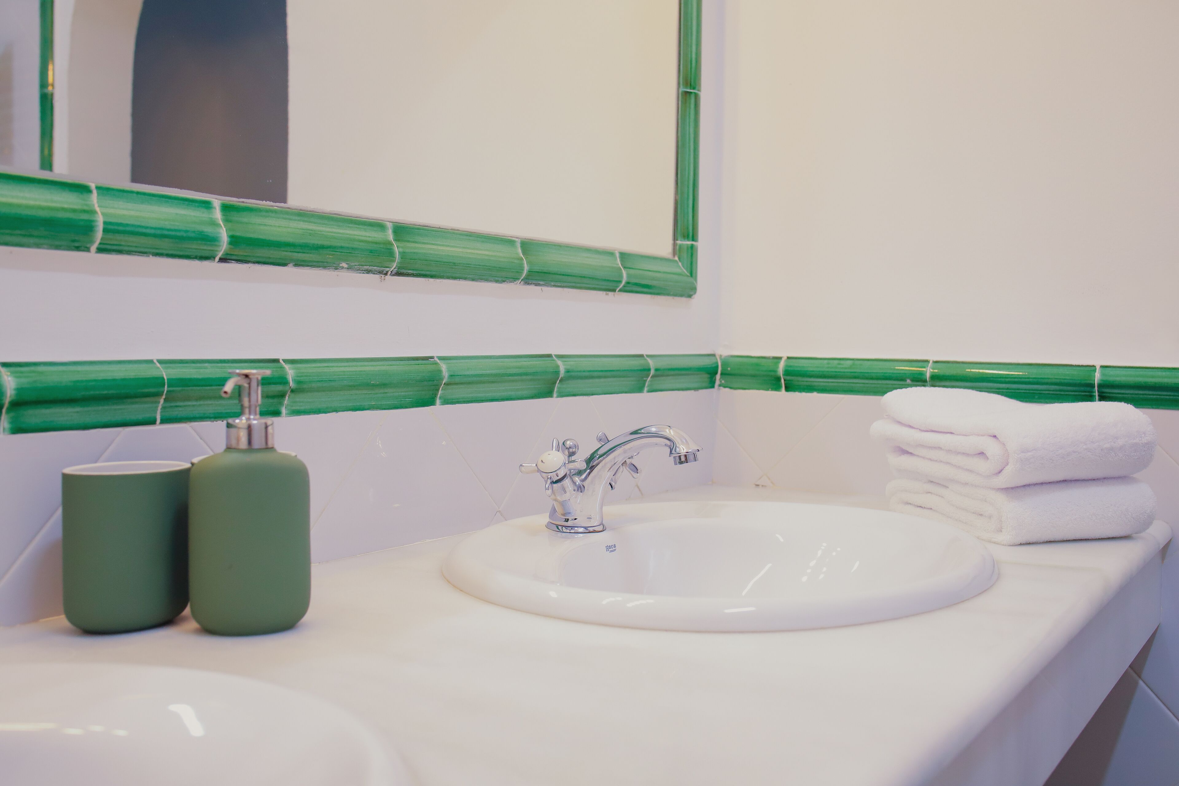A bathroom with a white sink, green-tiled wall, and a mirror above it.