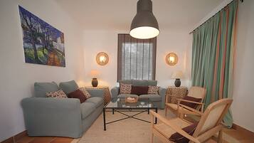 A living room with a sofa, armchairs, a coffee table, and a painting on the wall.