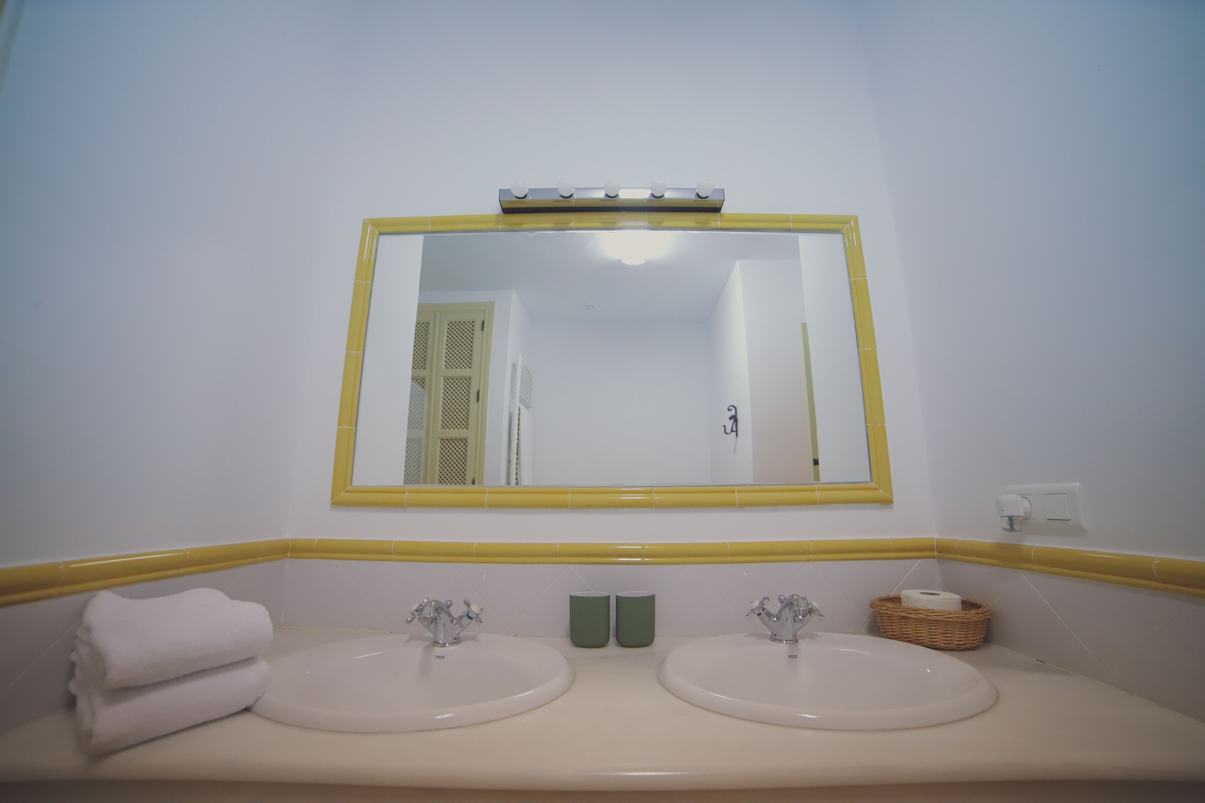 A bathroom with two sinks, a mirror, and a yellow-framed mirror.