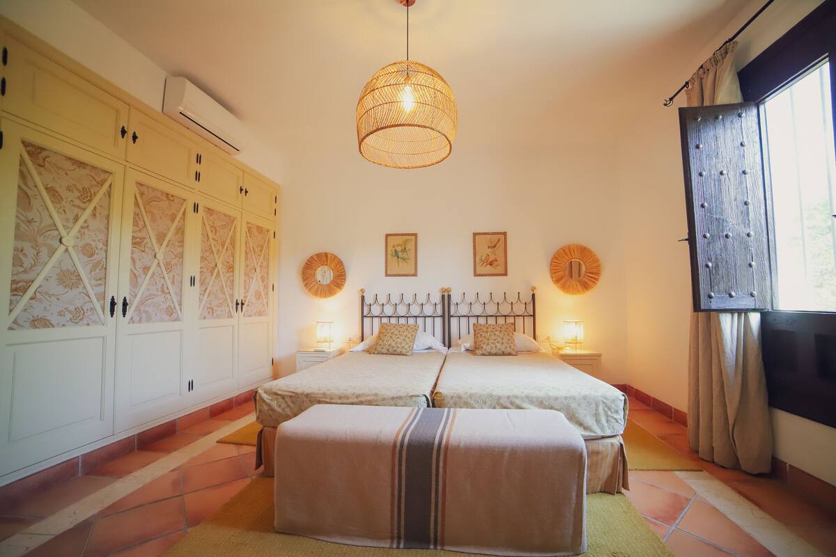 Une chambre avec deux lits, une grande armoire et un luminaire suspendu.