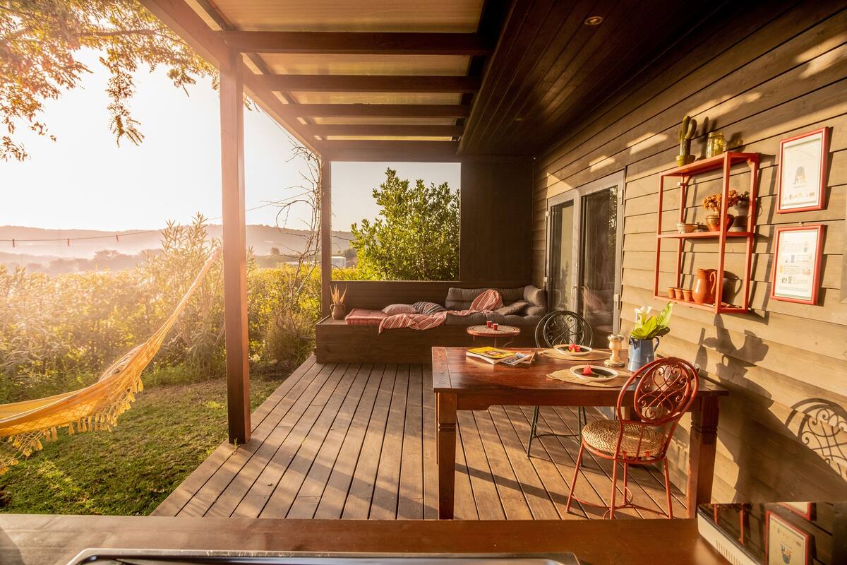A wooden deck with a hammock, a table with chairs, and a sofa with cushions.