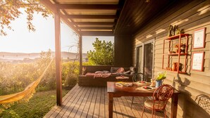 A wooden deck with a hammock, a table with chairs, and a sofa with cushions.