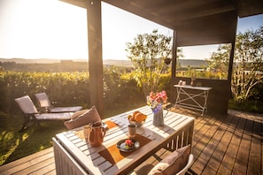 An outdoor patio with a wooden table set for two, a chair, a small table with a vase of flowers, and a view of a vineyard. - Gato Preto de Silves (Silves)