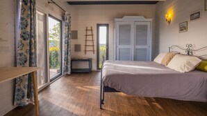 A bedroom with a bed, a wooden floor, a window with curtains, a door, and a ladder.