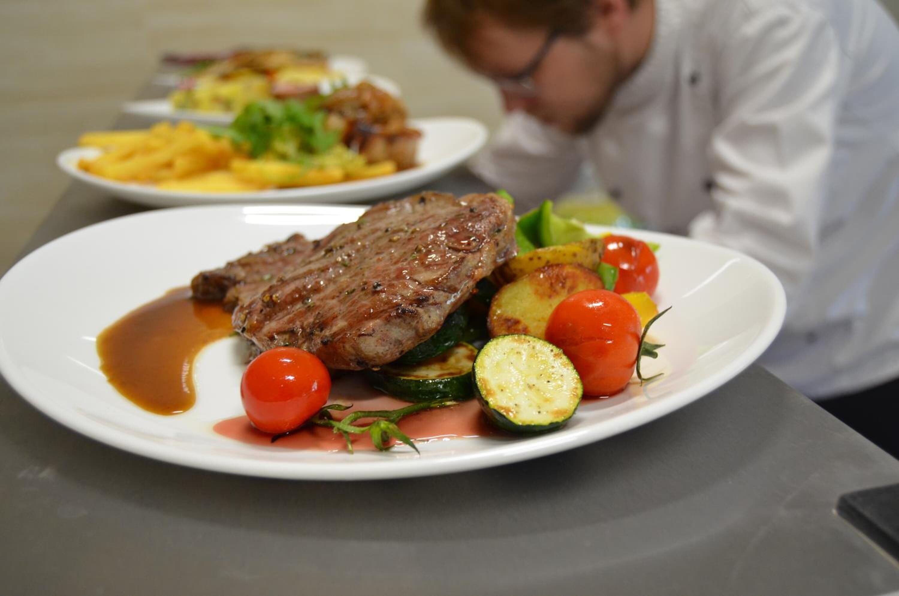 A dining table with plates of food, including steak and vegetables.