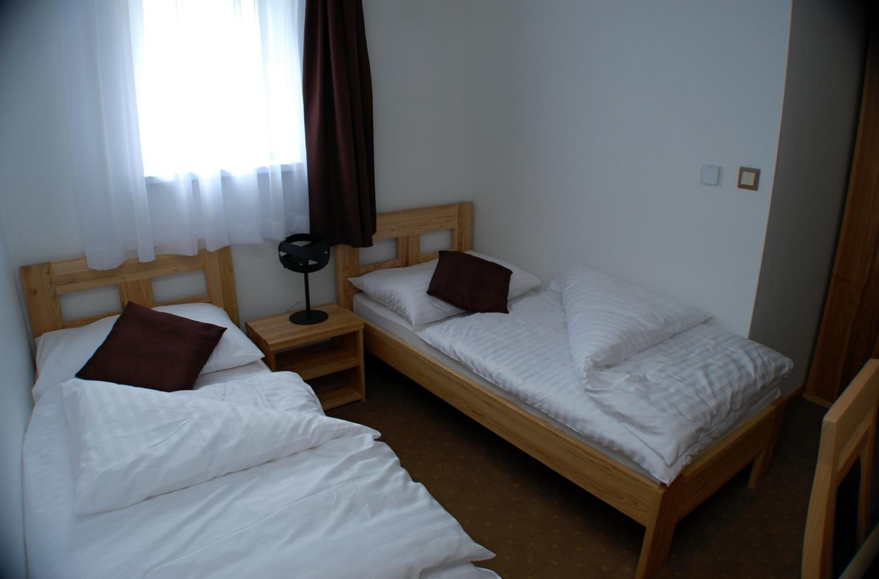 Een kamer met twee eenpersoonsbedden, een nachtkastje, een lamp en een raam met gordijnen.