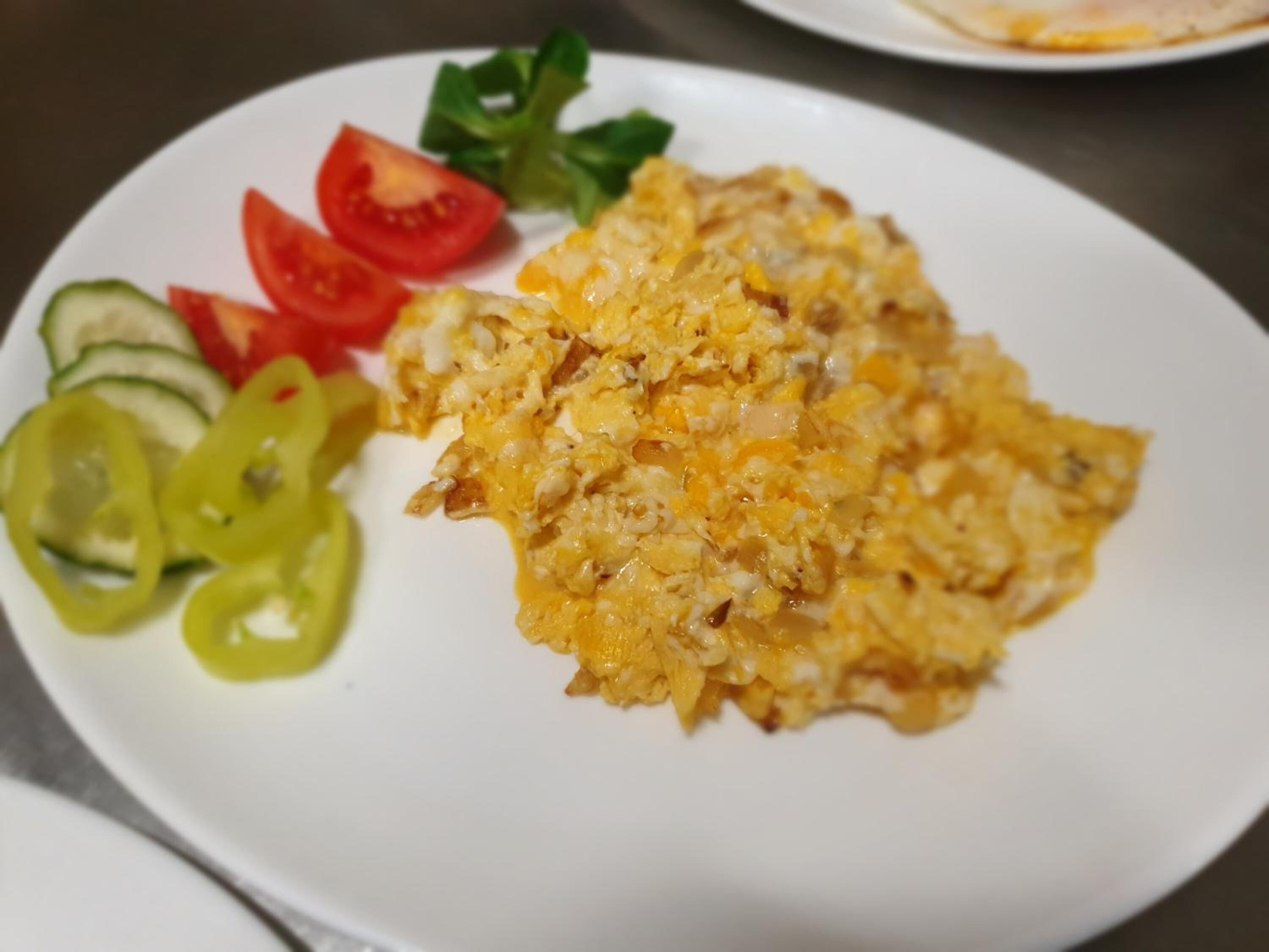Ein Teller mit Rührei, Tomatenscheiben, Gurkenscheiben und Paprikastreifen.