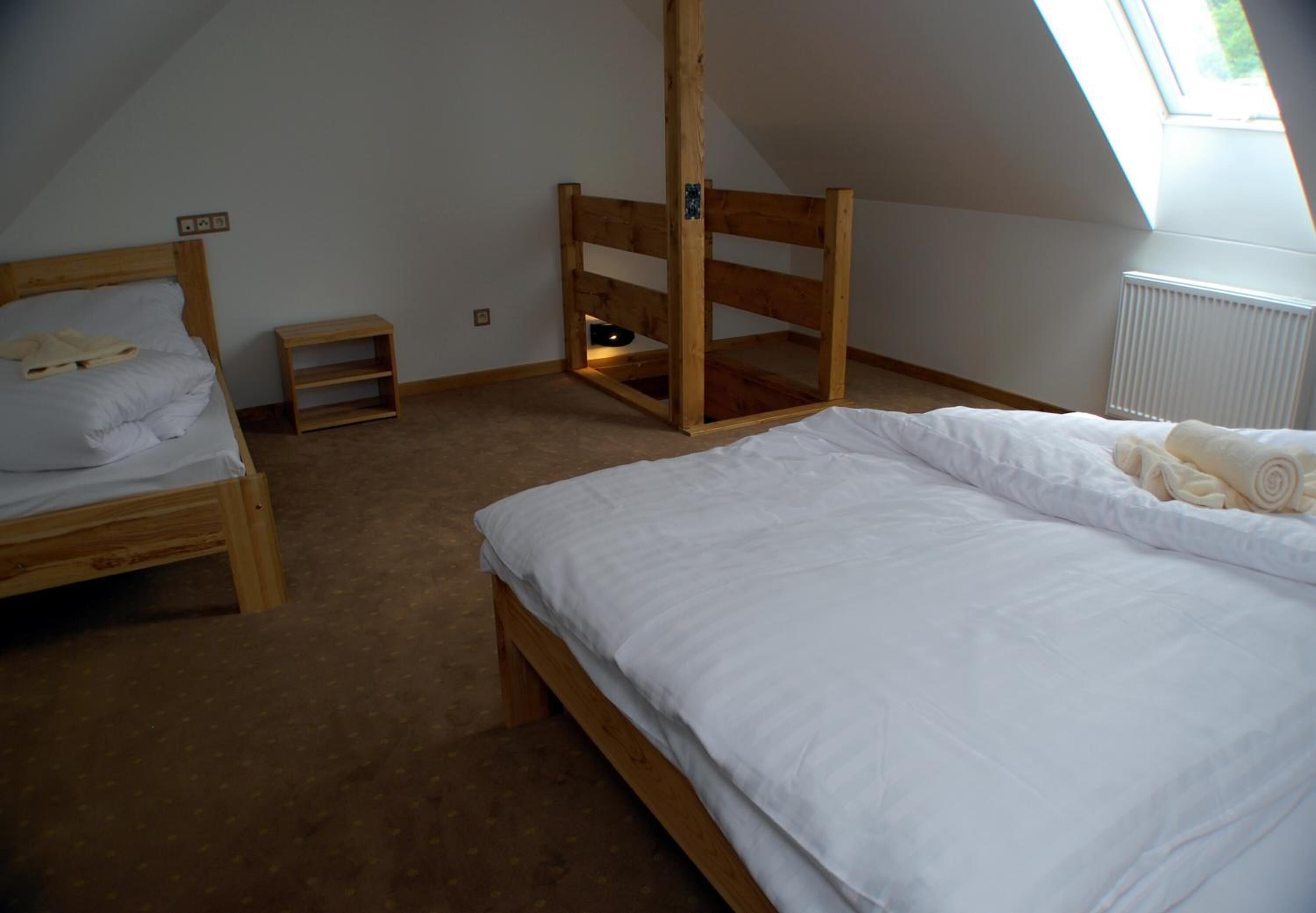 A bedroom with two wooden beds, a small wooden shelf, and a slanted ceiling.