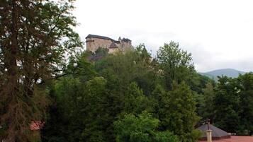 Vista de un castillo en una colina, rodeado de árboles y una furgoneta blanca estacionada cerca.