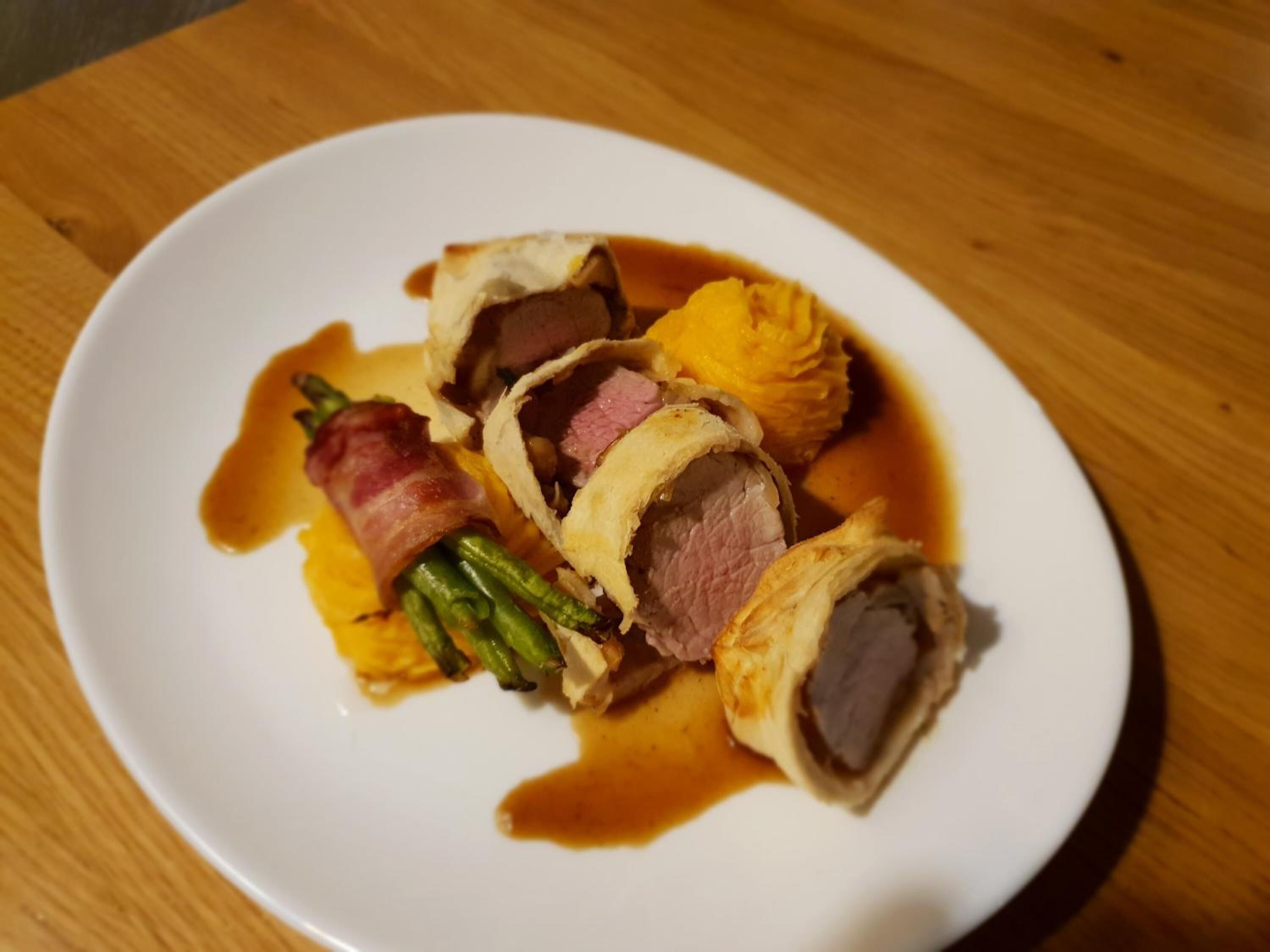 A plate with a rolled meat dish, possibly beef, accompanied by green beans and a yellow vegetable, possibly squash, on a white plate.