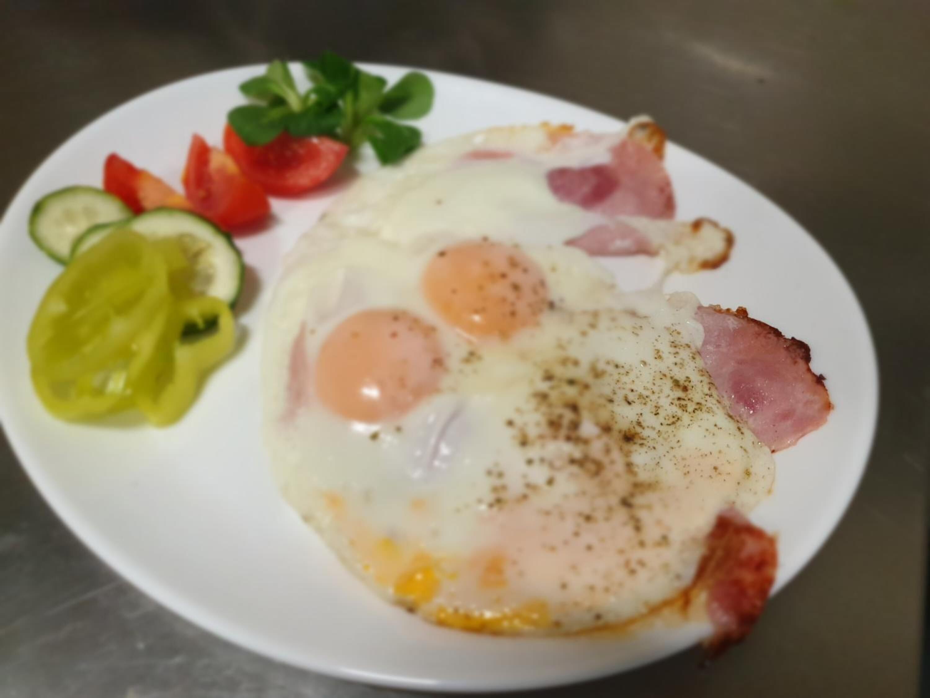 Un piatto con due uova al tegamino, prosciutto e verdure a fette.