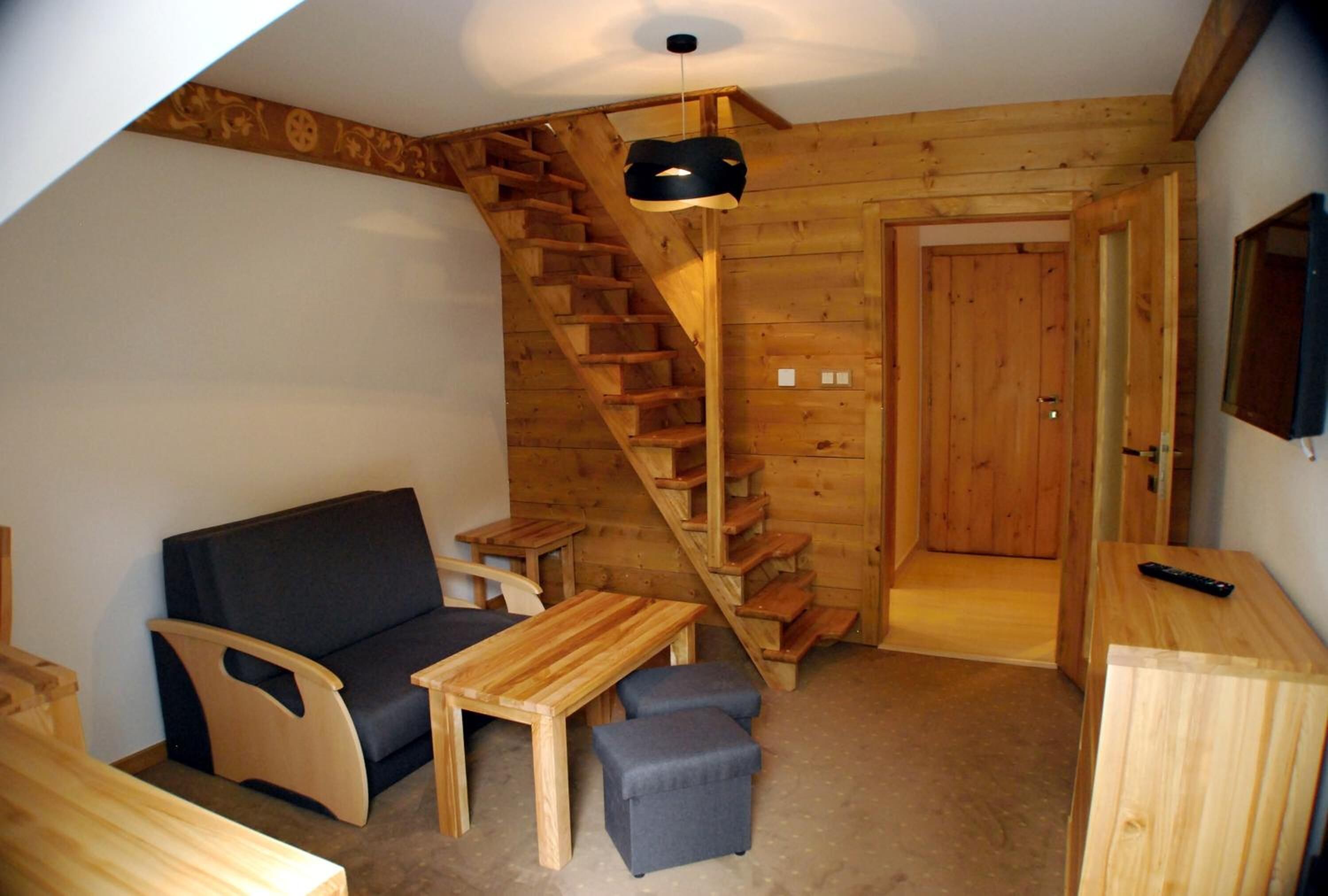 A wooden interior with a staircase, a sofa, a table, and a TV.