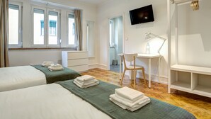 Ein Hotelzimmer mit zwei Betten, einem Schreibtisch, einem Stuhl, einem Fernseher und einem Kleiderschrank.