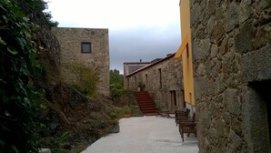 Um beco estreito com edifícios de pedra, uma escadaria que leva a um segundo andar e mesas ao ar livre.
