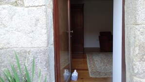 Paredes de pedra com uma porta de madeira que dá para um quarto com um tapete estampado e uma pequena mesa com uma caixa de lenços.