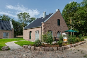 A brick house with a sloped roof, a paved driveway, and a garden area with a patio.