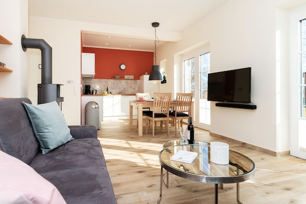 A modern living room with a sofa, a glass coffee table, and a TV mounted on the wall.