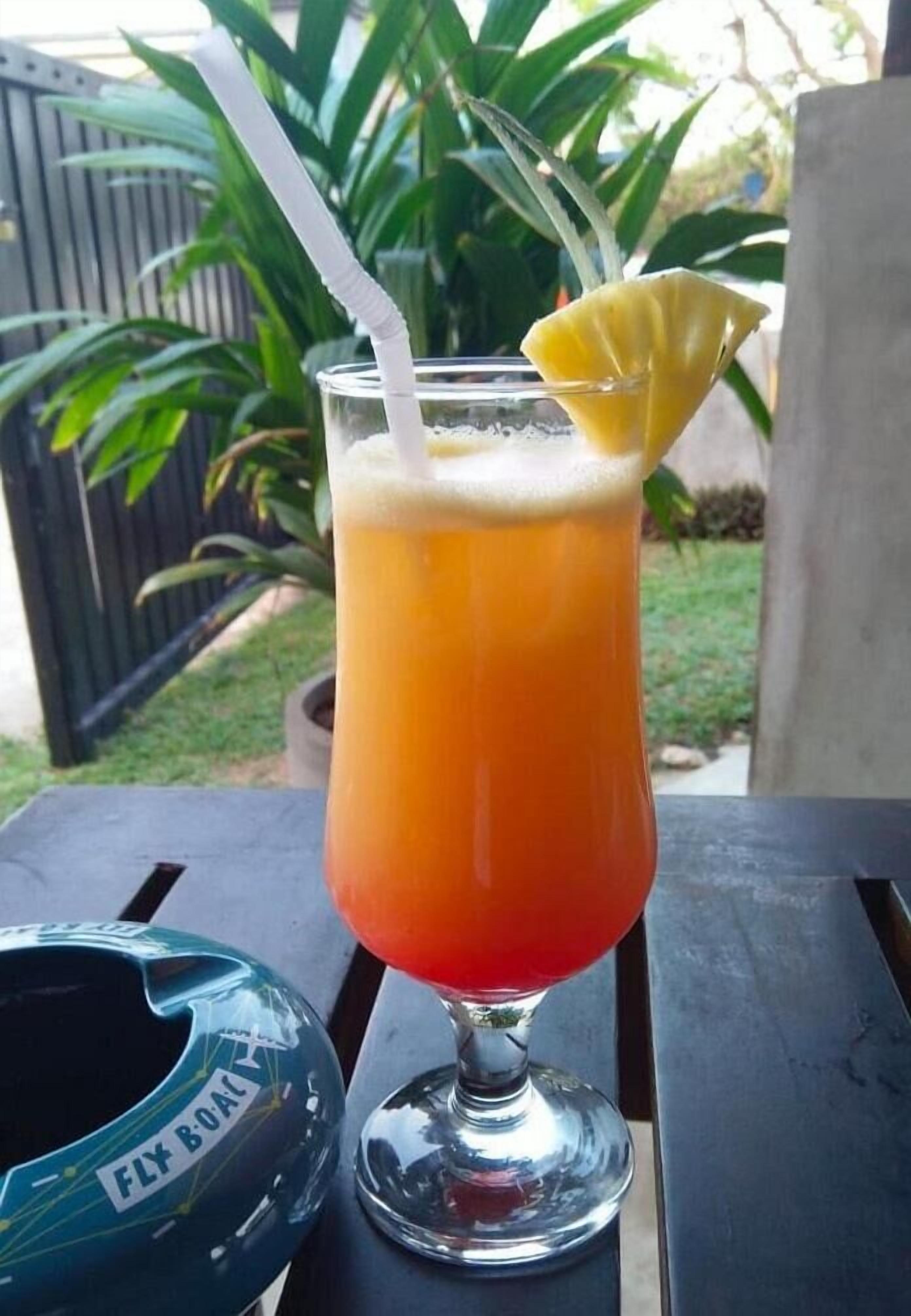 A tall glass with a layered drink, a straw, and a lemon wedge on a table.