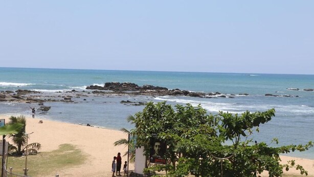 A beach with a rocky shoreline, a few people, and a tree in the foreground. - Rest House Tangalle (Tangalle)