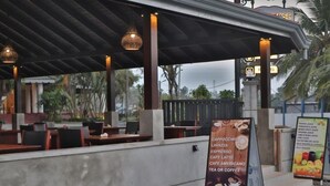 An outdoor cafe with tables and chairs, a sign listing menu items, and a covered seating area. - Rest House Tangalle (Tangalle)