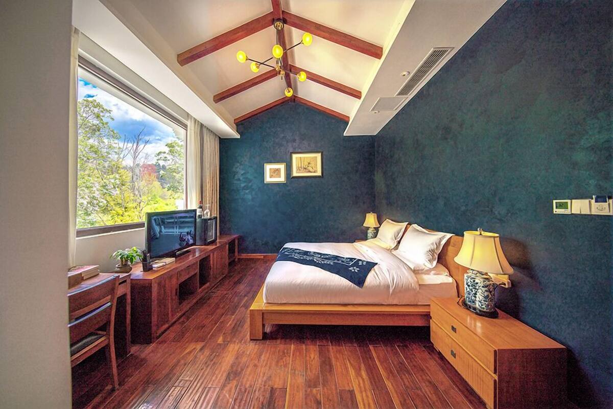 A bedroom with a large bed, wooden furniture, a desk, and a TV.