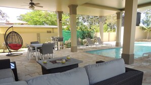 Un patio al aire libre con piscina, zona de estar y una silla colgante.