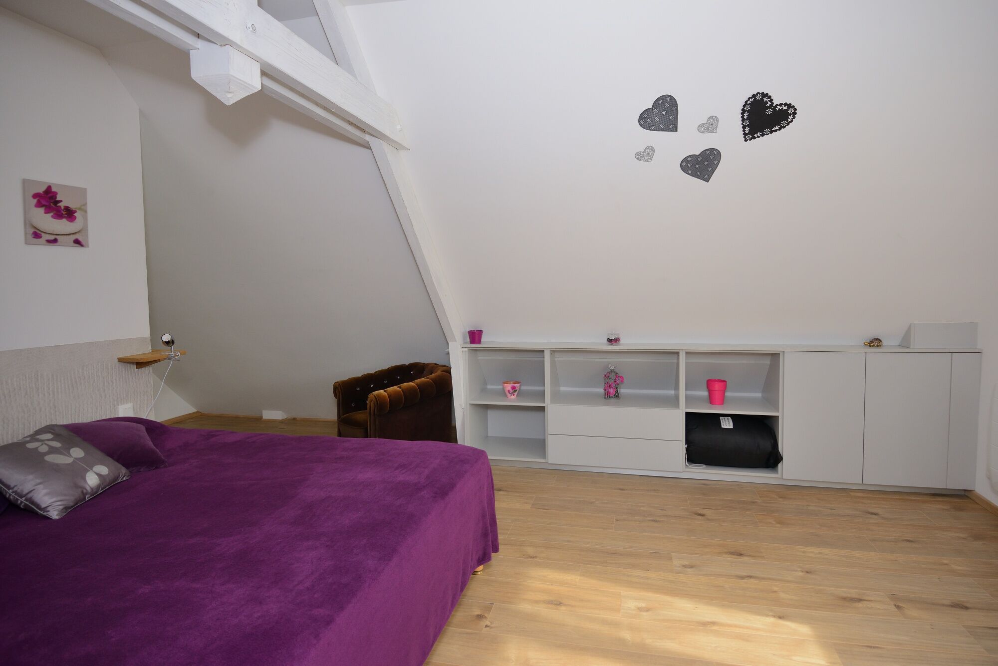 A bedroom with a purple bed, a white ceiling, and a white wardrobe with pink and black items.