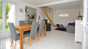 A modern interior with a wooden dining table, grey chairs, a staircase, and a living area with a sofa and a coffee table. - "Les 2 Marmottes" your charming gîte in Essonne (Buno-Bonnevaux)