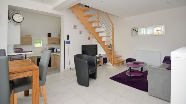 A modern living room with a wooden staircase, a dining area, and a kitchen. - "Les 2 Marmottes" your charming gîte in Essonne (Buno-Bonnevaux)