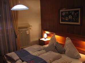 A hotel room with a bed, a nightstand with a lamp, a radiator, and a framed picture on the wall.