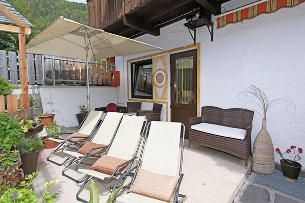 A patio with sun loungers, a wicker sofa, and a large umbrella.